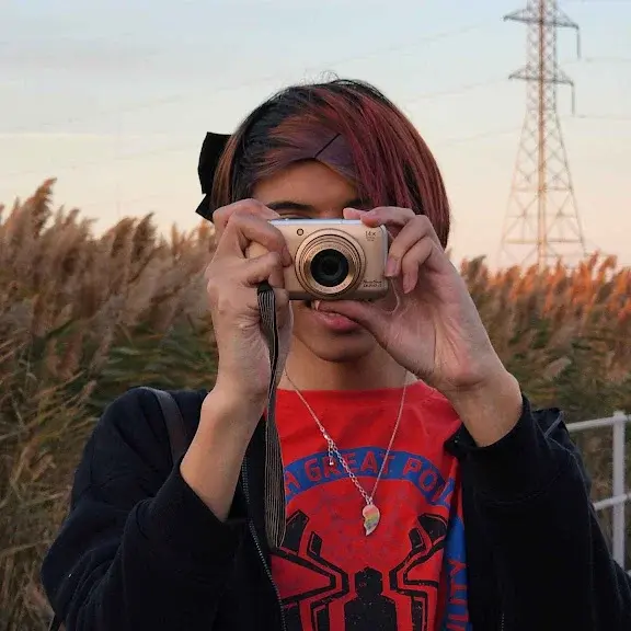 person with red hair pointing a digital camera towards you